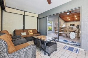 Un salon moderne avec des meubles en osier, une porte vitrée donnant sur la cuisine et un ventilateur de plafond.