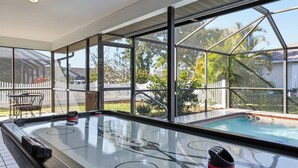 An indoor pool area with a glass enclosure, a pool table, and a view of the backyard. - Spacious 3BR Heated Pool Home-Pets OK-12 min to beach (Cape Coral)
