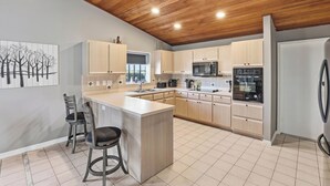 A modern kitchen with wooden ceiling, light-colored cabinets, and a central island with bar stools. - Spacious 3BR Heated Pool Home-Pets OK-12 min to beach (Cape Coral)