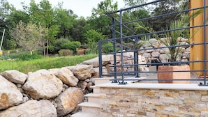 Una escalera de piedra que sube hacia una barandilla de metal, rodeada por un muro de piedra y follaje.