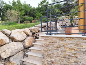 A stone staircase leading up to a metal railing, surrounded by a stone wall and greenery.
