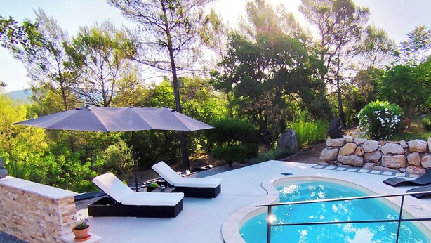 Una piscina con sillas de descanso y una sombrilla, rodeada de un muro de piedra y vegetación.