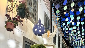 Une rue étroite, bordée de bâtiments des deux côtés, décorée de jardinières suspendues et d’une guirlande de petites lumières rondes bleues et blanches.
