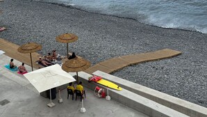Une zone de plage avec une promenade en bois, des parasols et des gens qui se détendent.