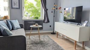 Ein modernes Wohnzimmer mit einem grauen Sofa, einer weißen TV-Konsole und einem kleinen runden Tisch.