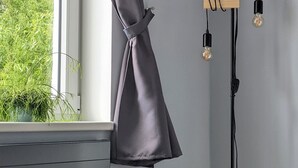 Ein runder Tisch mit weißer Tischplatte und Holzbögen, ein grauer Teppich, eine Stehlampe mit drei Lampenschirmen und ein Fenster mit Vorhang.