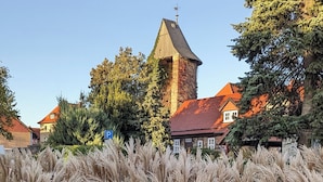 Ein traditioneller Steinturm mit rotem Dach, umgeben von Häusern und hohen Bäumen.