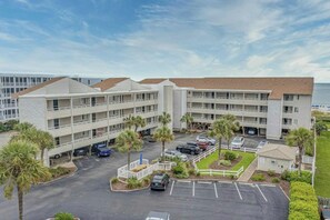 A multi-story hotel with a parking lot, palm trees, and a view of the ocean. - Pelican's Watch 211- 3 Bedroom- Outdoor Pool (Myrtle Beach)