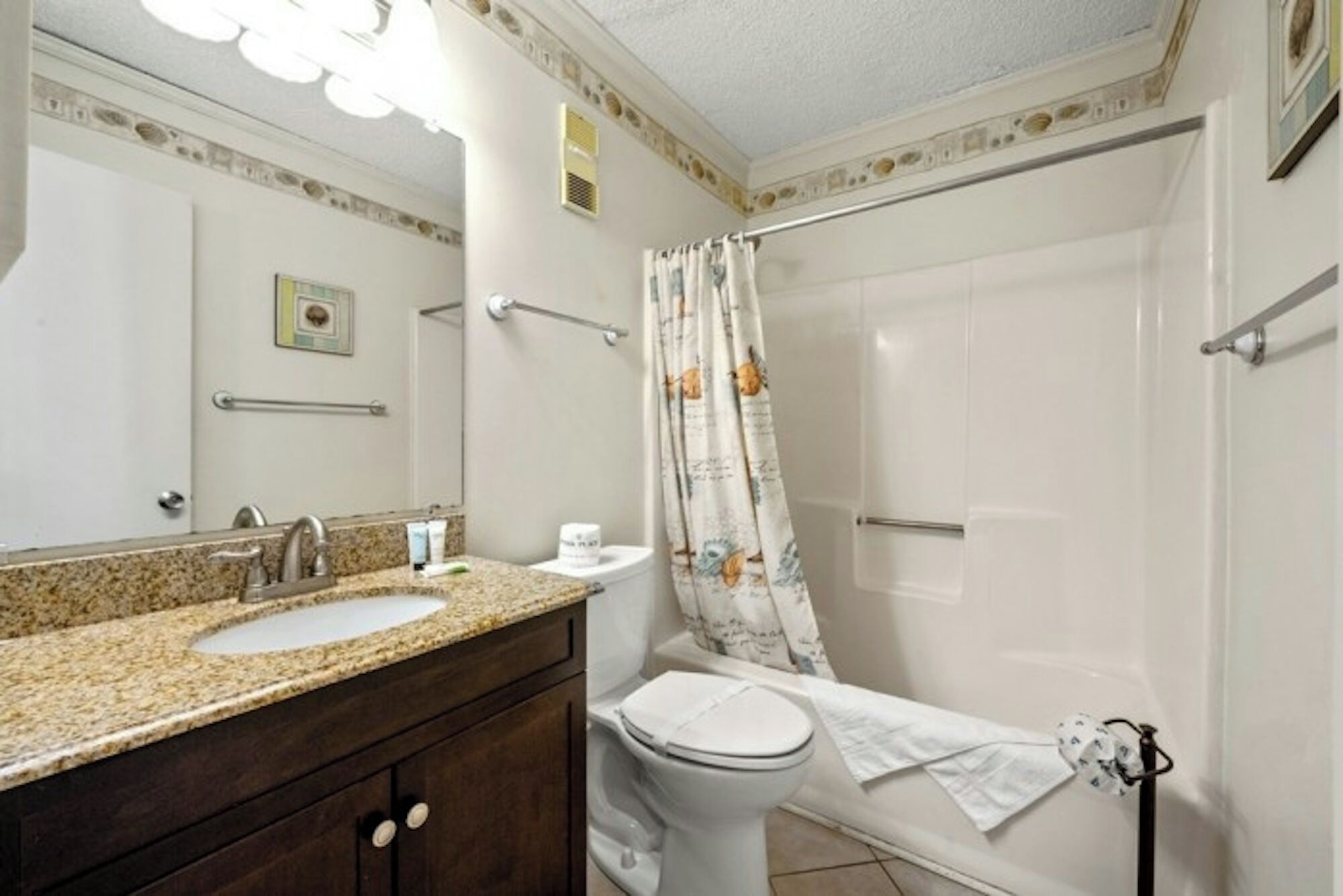 Ein Badezimmer mit Granitwaschtisch, Toilette und Duschkabine mit Vorhang.