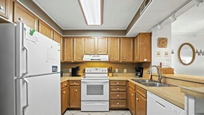 Une cuisine de taille réduite, avec des meubles en bois, un réfrigérateur blanc, une cuisinière et un lave-vaisselle.
