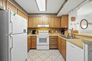 A compact kitchen with wooden cabinets, a white refrigerator, a stove, and a dishwasher. - Pelican's Watch 211- 3 Bedroom- Outdoor Pool (Myrtle Beach)