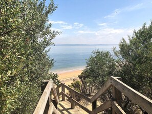 Eine Holztreppe führt zu einem Strand mit blauem Himmel und ruhigem Wasser.
