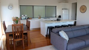 Uma cozinha moderna com uma ilha central, um espaço de refeições com cadeiras de madeira e um sofá cinza.