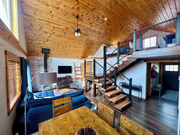 Un vaste espace de vie doté d’un plafond en bois, d’un canapé bleu, d’une table à manger en bois et d’un escalier menant à un niveau supérieur.