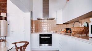 Una cocina moderna con armarios blancos, horno integrado y zona de comedor con mesa de vidrio y sillas de madera.