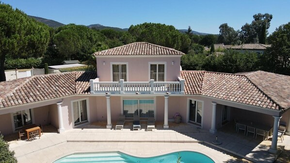 Una casa a due piani con piscina, portico coperto e vista sul paesaggio circostante.