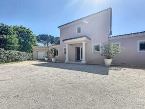 Una casa a due piani con vialetto sterrato, piante in vaso e cielo sereno.