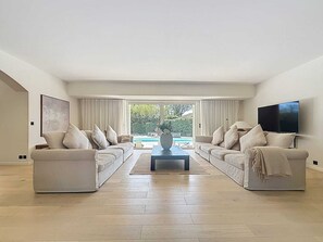 A spacious living room with a large TV, two sofas, a coffee table, and a view of a swimming pool. - Stunning villa with a heated pool and a view of Grimaud Castle (Grimaud)