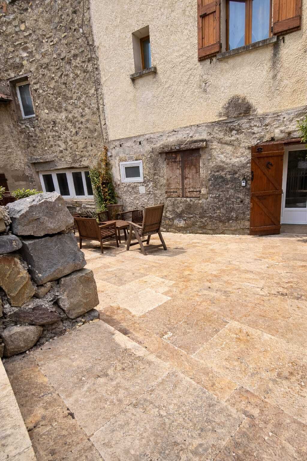 A courtyard with stone flooring, a wooden table with chairs, and a stone wall.