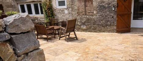 A courtyard with stone flooring, a wooden table with chairs, and a stone wall.