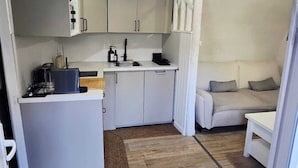 Una cocina compacta con muebles blancos, una isla central y una lámpara colgante.