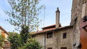 Un patio de piedra con mobiliario exterior, una pared de piedra y un edificio rústico con contraventanas de madera.