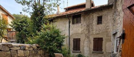 A stone patio with outdoor furniture, a stone wall, and a rustic building with wooden shutters.