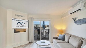 A living room with a sofa, a coffee table, and a TV. There is a sign that says "BEACH HOUSE" and another that says "OCEAN CITY VACATION HOMES". - Harbour Bay 5, Beautiful 3BR Modern Bayside Townhome, Quiet! (Ocean City)