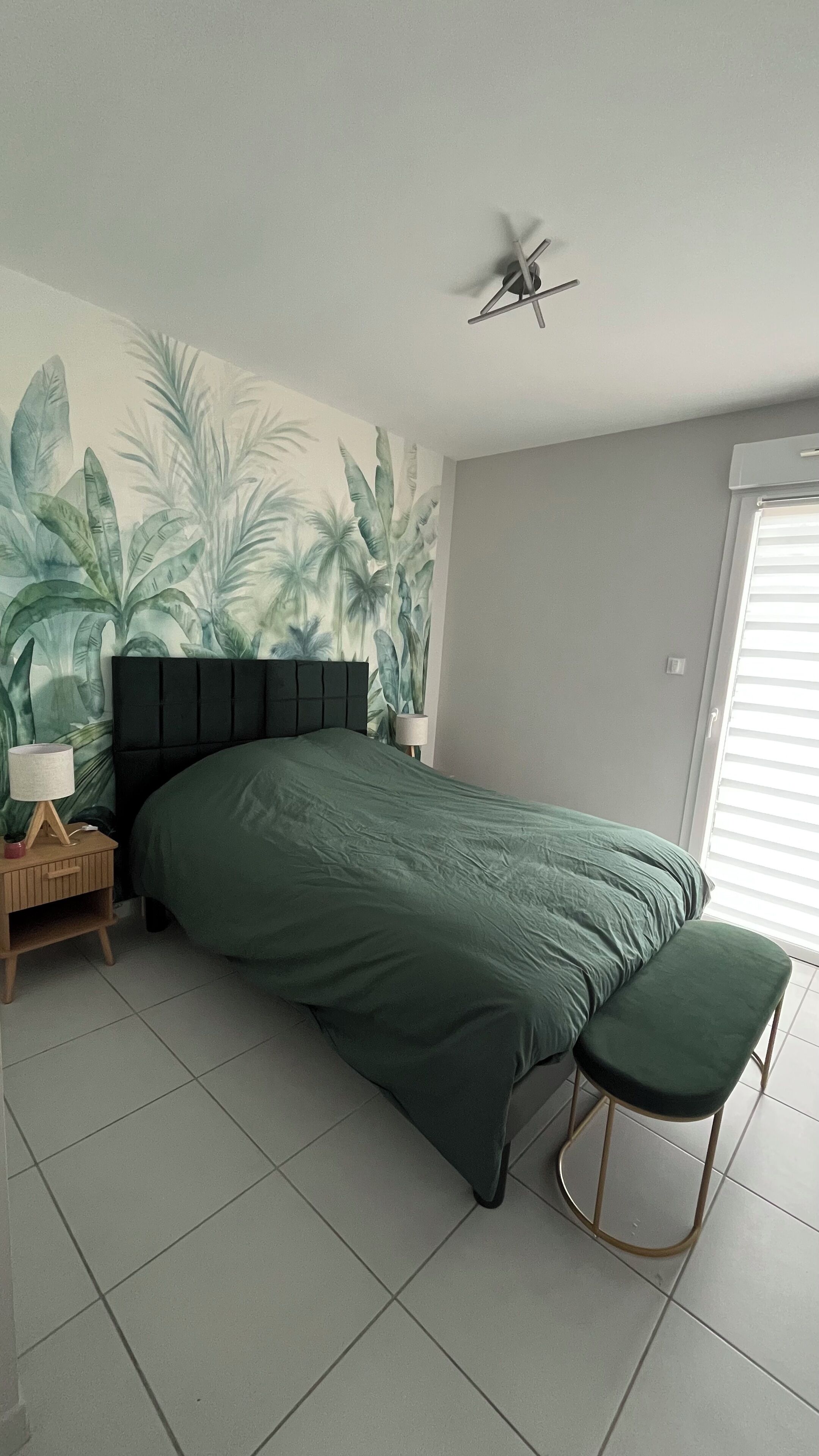 A bedroom with a bed, a bench, a nightstand, a lamp, and a ceiling fan.