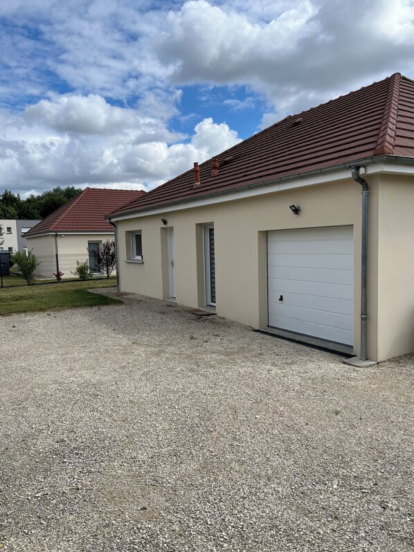 A two-story building with a red-tiled roof, a white garage door, and a gravel driveway. - "LE FAIRWAY - Single-family home, single-story, 96 m², 5 minutes from Troyes (Bréviandes)