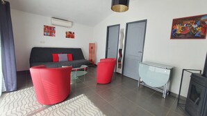 Uma sala de estar moderna com sofá, cadeiras vermelhas, mesa de vidro, televisão e obras de arte nas paredes.
