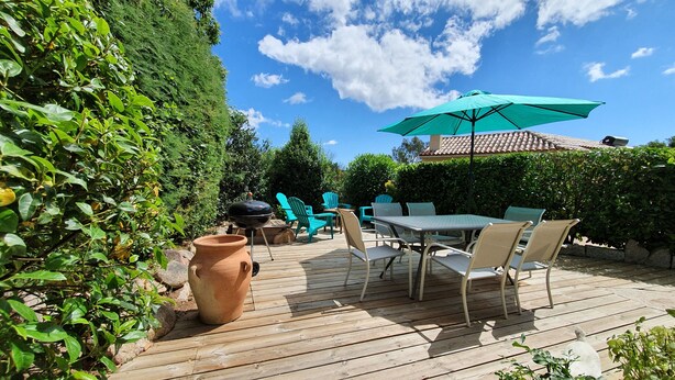 Um deck de madeira com móveis de exterior, churrasqueira e um grande guarda-sol.