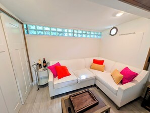 A white sectional sofa with colorful cushions, a small side table with a bottle, and a wooden coffee table. - Beach House, Modern Old Town Studio Near Duval - New Listing Discount! (Key West)
