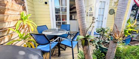 Un patio con mesa y sillas, rodeado de plantas y una terraza de madera.