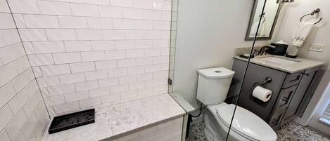 Ein modernes Badezimmer mit weißen, rechteckigen Fliesen, einer Marmorarbeitsplatte, einer Toilette, einem Waschbecken mit Spiegel und Fliesenboden mit Muster.