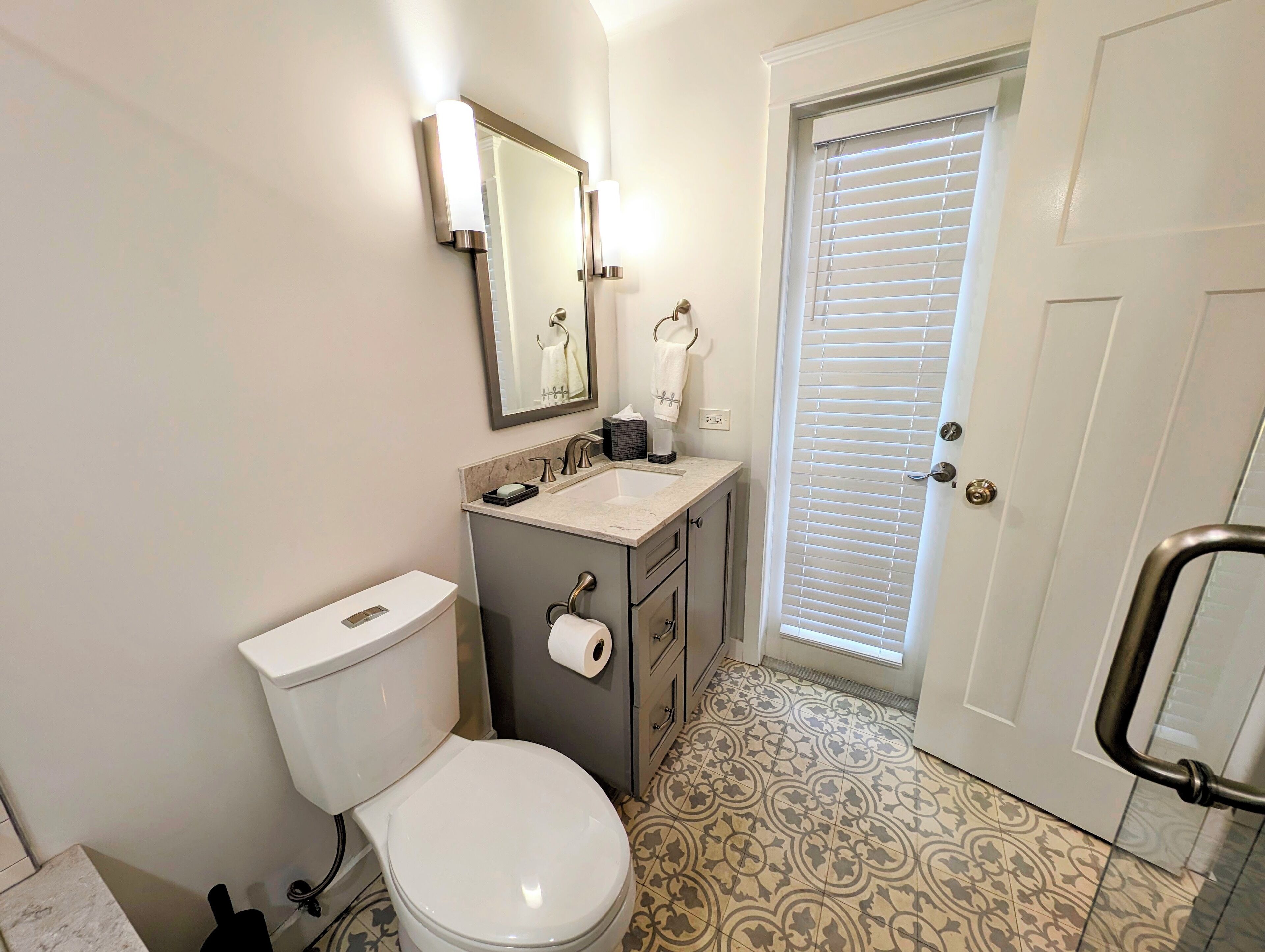 A bathroom with a toilet, sink, mirror, and a door with a window.