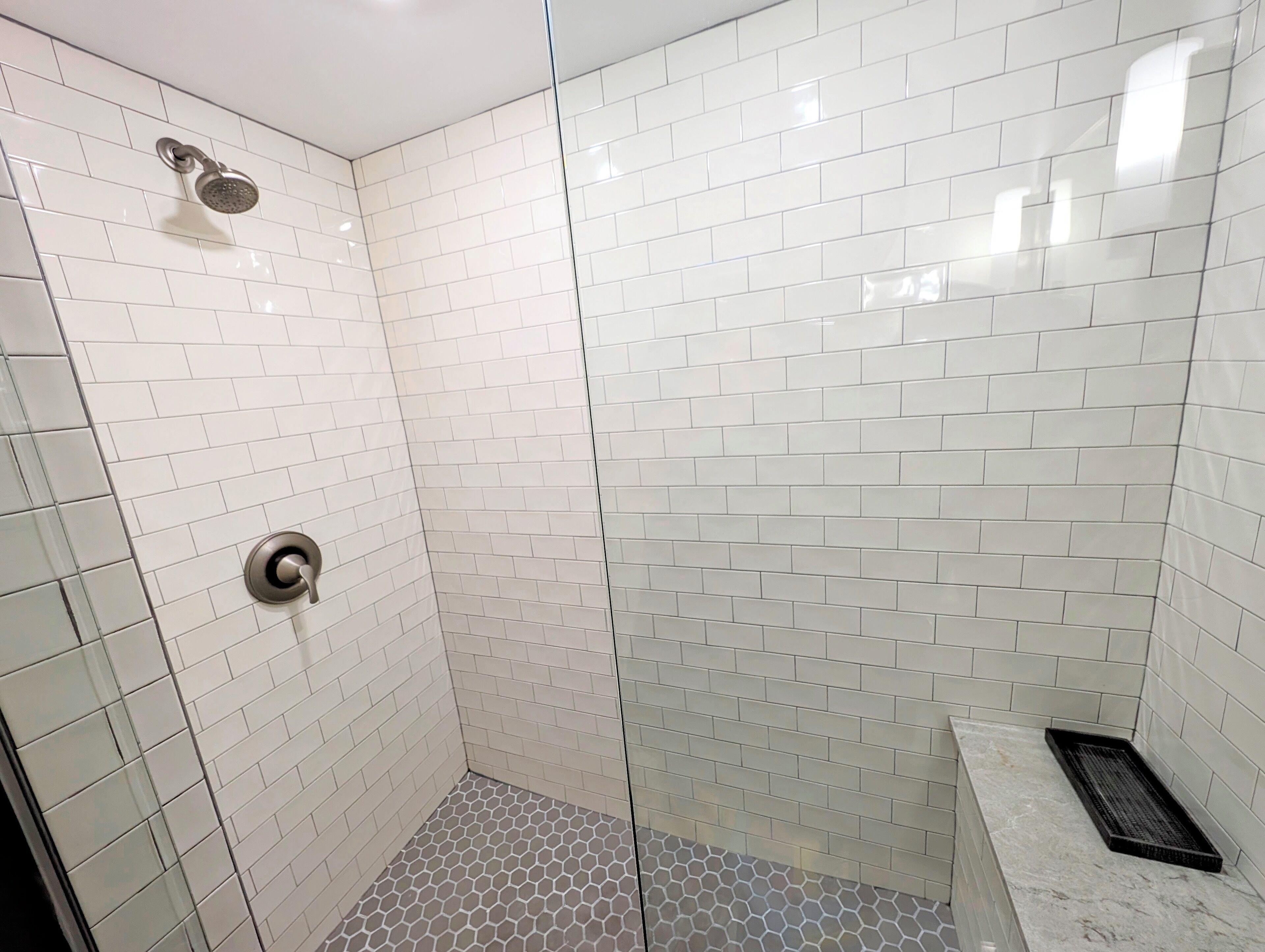 A shower with white tiles, a glass door, and a metal showerhead.