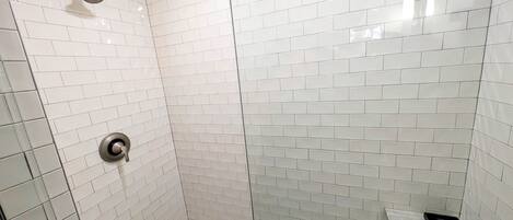 A shower with white tiles, a glass door, and a metal showerhead.