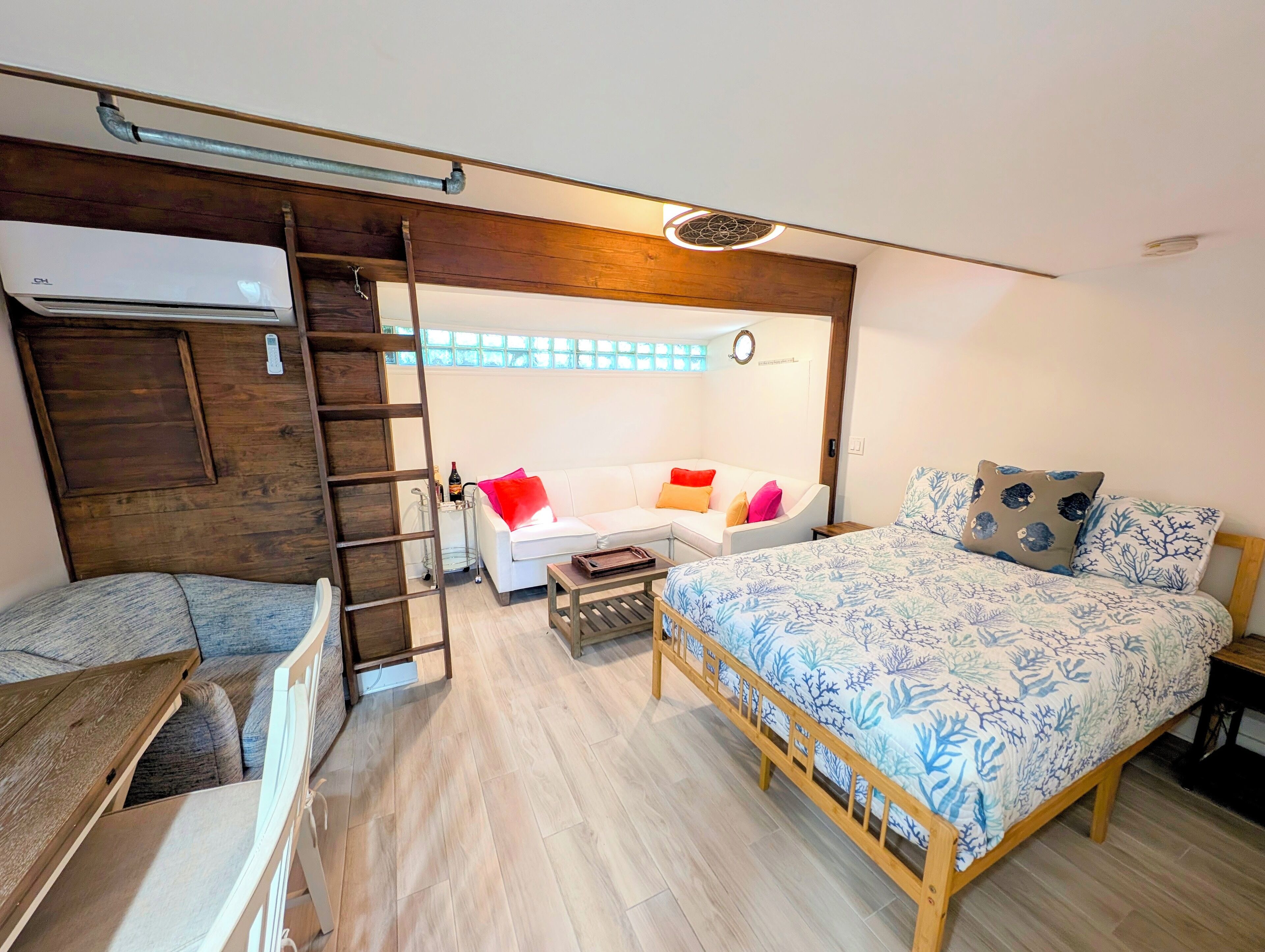 A compact room with a bed, a sofa, a ladder, and a small table.