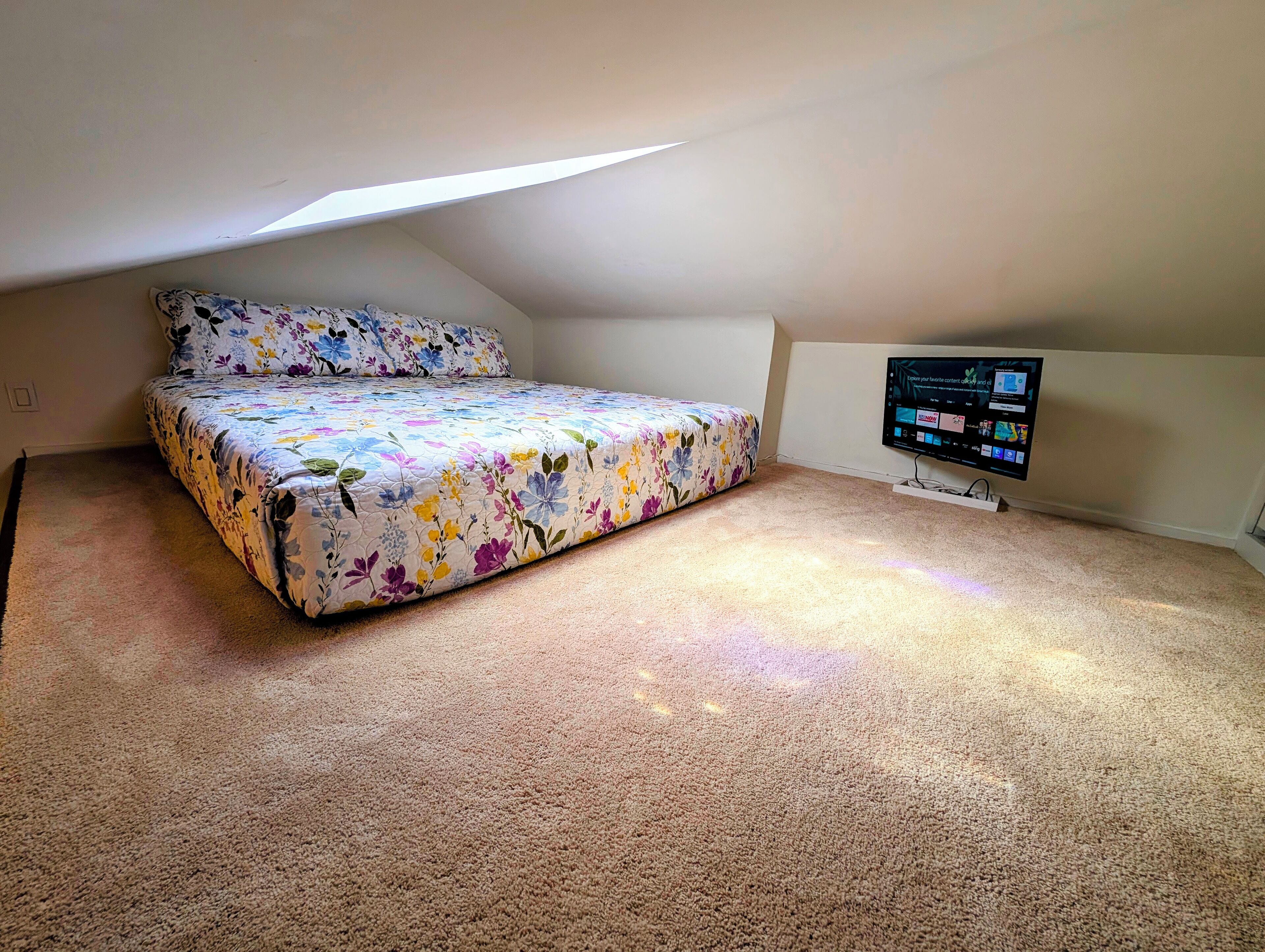 A bedroom with a bed, a television, and a sloped ceiling.