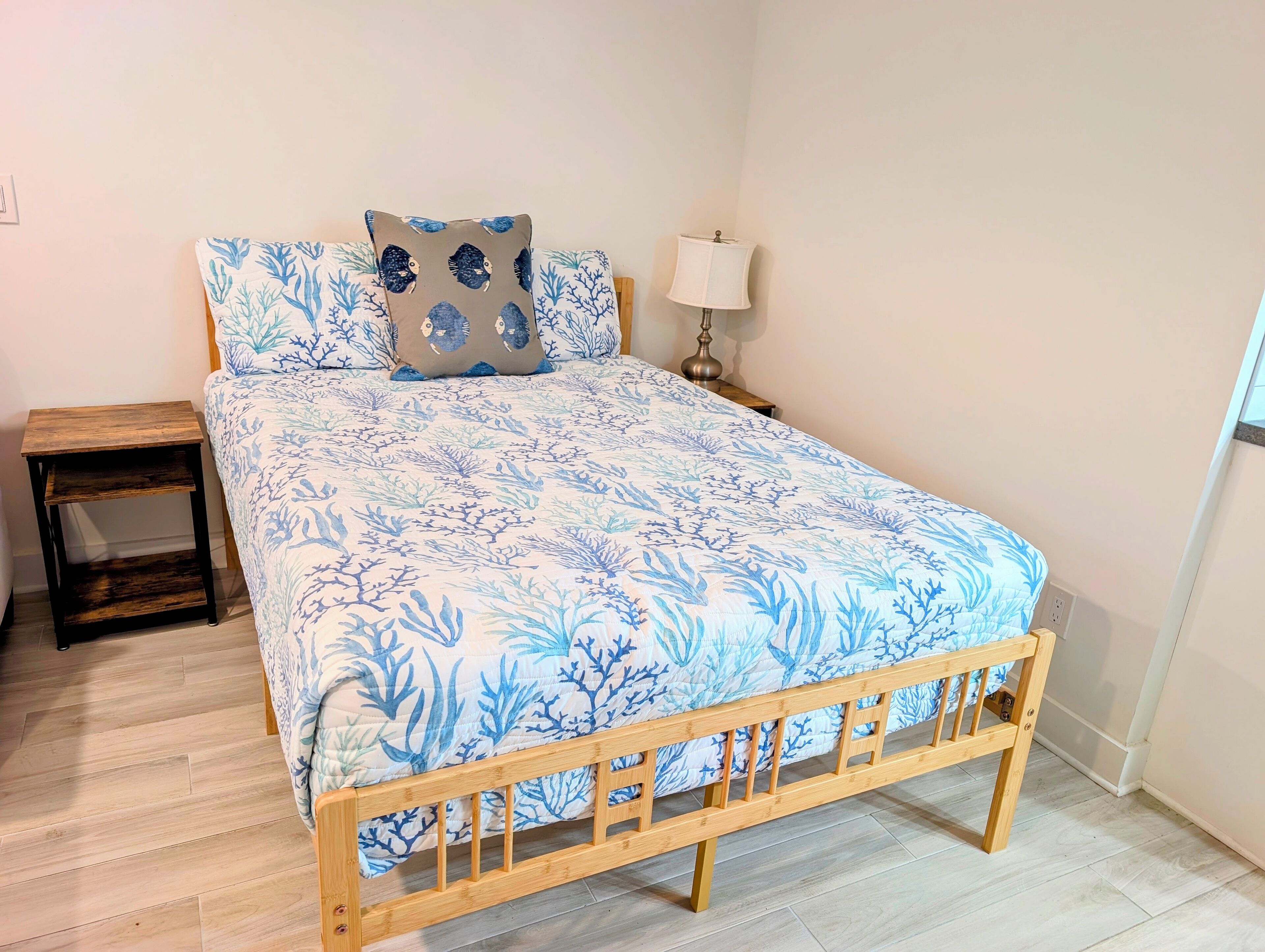 A bed with a blue and white coral pattern, a wooden headboard, a nightstand, and a bedside lamp.