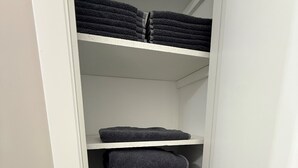 A white closet with shelves holding folded dark-colored towels. - Ann's Adobe - 2 Bdrm Apartment in Mansfield, OH - close to Lexington & Ontario (Mansfield)
