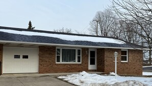 A single-story brick house with a white garage door, a front door, and a small window. - Ann's Adobe - 2 Bdrm Apartment in Mansfield, OH - close to Lexington & Ontario (Mansfield)