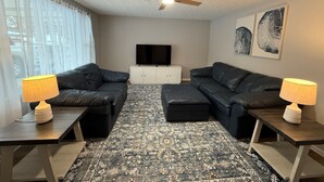 A living room with two black leather sofas, a patterned rug, a ceiling fan, a flat-screen TV, and artwork on the wall. - Ann's Adobe - 2 Bdrm Apartment in Mansfield, OH - close to Lexington & Ontario (Mansfield)
