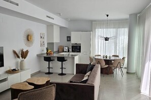 A modern living room with a sofa, coffee table, and dining area with chairs. - Villa LUISA La Marina Alicante with private pool 3 bedrooms & 3 bathrooms (VC)