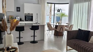 Una cucina moderna con mobili bianchi, un'area pranzo con un tavolo rotondo e sedie, e un soggiorno con divano e tavolino.