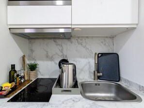 Eine moderne Küche mit einer schwarzen Induktionskochplatte, einer Edelstahl-Spüle und einer Marmor-Spritzschutzwand.