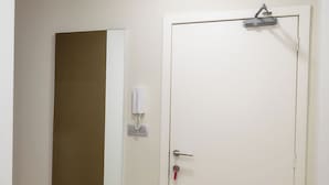 Une pièce avec un plancher en bois, une porte blanche avec une clé dans la serrure, un téléphone fixé au mur et une table avec des assiettes et des bols.