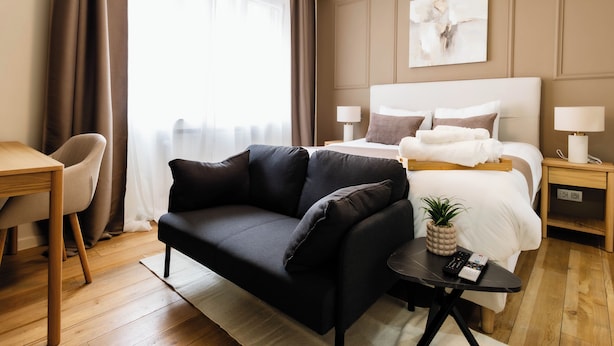 Une chambre d’hôtel moderne équipée d’un lit, d’un canapé, d’un bureau et d’une petite table avec une télécommande.