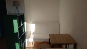 Ein kleiner, kompakter Raum mit einem Einzelbett, einem Holztisch und einer grünen Regalwand.